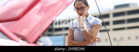 Nachdenkliche Frau schaut sich den Automotor aus der Nähe an Stockfoto