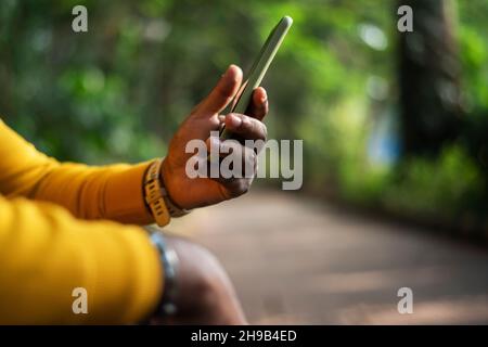 Eine Person, die ein Smartphone auf grünem Bokeh-Hintergrund verwendet, eine männliche Hand, die ein Smartphone hält Stockfoto