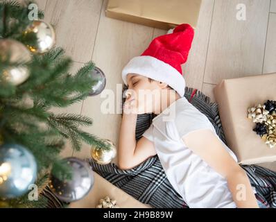 Der Junge liegt unter dem Baum und träumt. Weihnachtsbaum im großen Wohnzimmer. Stockfoto