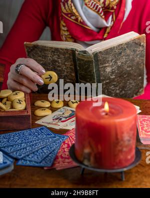 Ein in Rot gekleideter Wahrsager liest Karten und ein altes Buch, um die Zukunft vorherzusagen Stockfoto