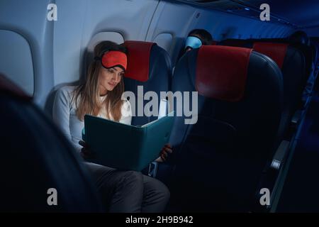 Frau in der Flugzeugkabine, die sich das Buch vor ihr ansieht Stockfoto