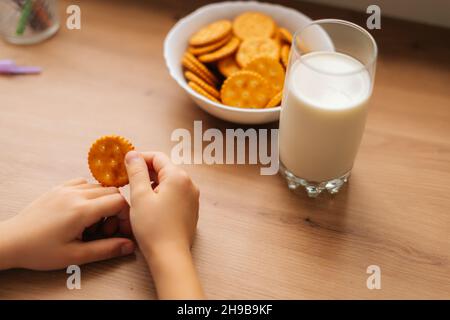 Nahaufnahme eines unerkennbaren kleinen Mädchens, das mit einem Glas Milch am Tisch einen Cookie hält, pov. Stockfoto