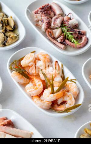 Auswahl an Fischgerichten. Meeresfrüchte auf einem Teller. Auf einem weißen Holzhintergrund. Selektiver Fokus Shrimp. Garnelen, Lakerda, Oktopus-Salat, Muscheln mit Marinade Stockfoto