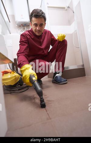 Fokussierter Arbeiter in Gummihandschuhen Dampfreinigungsfuge zwischen Keramikfliesen Stockfoto