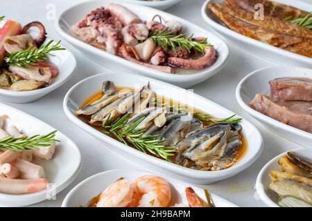 Auswahl an Fischgerichten. Meeresfrüchte auf einem Teller. Auf einem weißen Holzhintergrund. Selektiver Fokus marinierte Sardellen. Lakerda, Kraken-Salat, Garnelen, Fischsalat Stockfoto