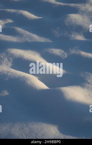 Bei sonnigem, frostigen Wetter ein Fragment einer verschneiten, hügeligen Oberfläche mit kleinen, vertikalen Gruben Stockfoto