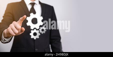 Geschäftsmann im Anzug hält Metallgetriebe und Zahnräder Mechanismus der Interaktion Teamarbeit Konzept, Hand halten Gruppe von virtuellen Zahnräder Rad. Stockfoto