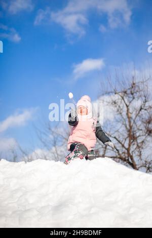 Kleines Mädchen spielt Schneebälle. Kind hat Spaß an sonnigen Wintertag, spielt und reitet Schneerutsche ohne Schlitten und springt in Schneeverwehungen, Winter Stockfoto