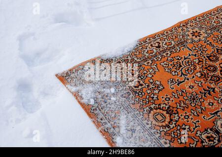 Teppich lügt onsonnow. Der alte persische Teppich in roten Farbtönen wird auf den Kopf gestellt und mit Schnee bestreut, um ihn zu reinigen Stockfoto