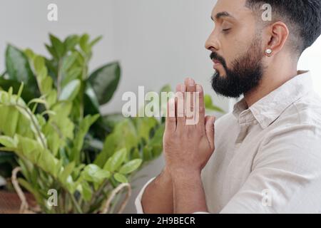 Schöner bärtiger Mann, der mit namastigen Händen betet, Augen schließt und atmet Stockfoto