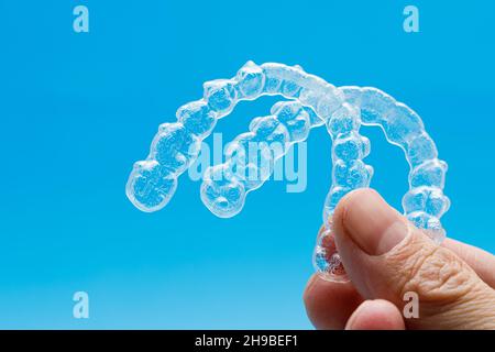 Hand mit zwei transparenten Haltern auf blauem Hintergrund. Invisalign Kieferorthopädie Konzept Stockfoto