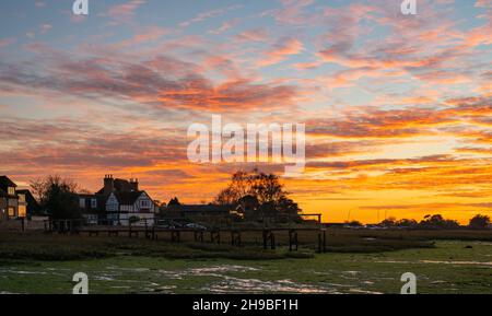 Schöner, wolkig-oranger Himmel nach Sonnenuntergang über Bosham Quay (Bosham Creek) im Chichester Harbour bei Ebbe im Winter in West Sussex, England, Großbritannien. Stockfoto