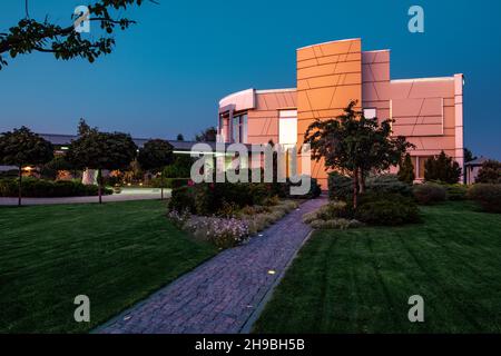 Blick in die Dämmerung auf das moderne Landhaus und die gepflegte angrenzende Grünanlage im Sommer Stockfoto