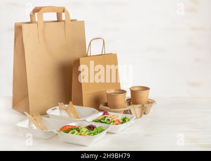 Lieferung von Lebensmitteln. Papiertüten, Lunchboxen mit Salat und Kaffee auf weißem Holzhintergrund. Speicherplatz kopieren. Stockfoto
