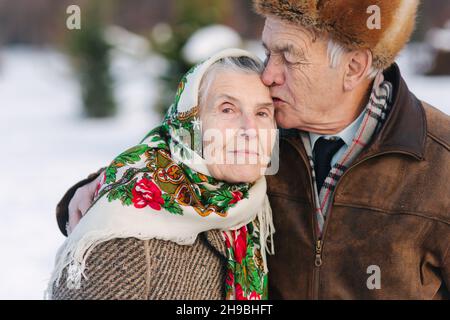 Porträt eines älteren Ehepaars. Älterer Mann küsst seine Frau in gewichtigen. Altes Paar zu Fuß im Park im Winter Zeit. Frohe Familie. Goldene Hochzeit Stockfoto