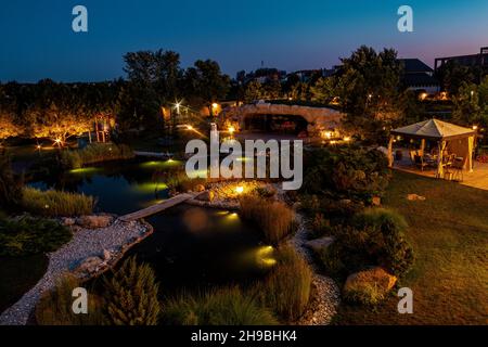 Innenhof des Landhauses mit Terrasse und künstlichem Teich mit Beleuchtung im Sommerabend Stockfoto