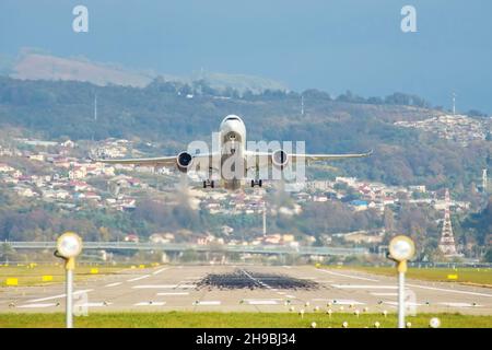 Passenger Jet, der von einer Start- und Landebahn mit Häusern auf dem Hang dahinter abfliegt Stockfoto