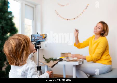 Eine junge Mutter und ihre Tochter nehmen gemeinsam einen Videostream auf. Ein kleines Mädchen hilft ihrer Mutter, einen Vlog aufzunehmen. Das Konzept des Video-Streamings. Stockfoto