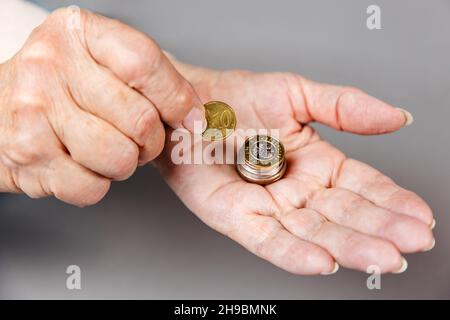 Nahaufnahme von Frauen mit faltigen Händen, die eine Euro-Münze in einen Münzstapel gelegt haben. Grauer Hintergrund. Das Konzept der Altersvorsorge und Altersvorsorge. Stockfoto