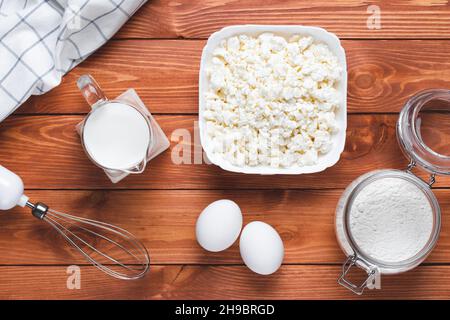 Backzutaten zum Kochen auf einem braunen Holztisch. Eier, Mehl, Quark und Milch auf einem Brett, Lebensmittelhintergrund. Draufsicht, flach liegend Stockfoto