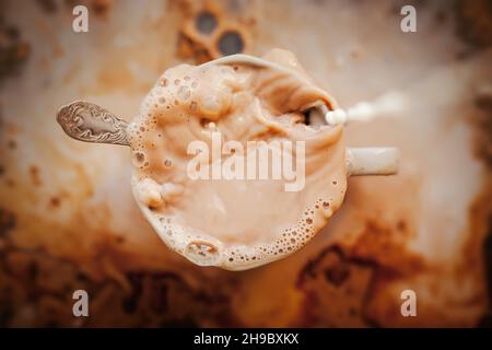Der Mensch goss Milch in einen Kaffeebecher. Chaos in der Küche. Ein angenehmer belebender Drink zum Frühstück. Eiskaffee. Stockfoto
