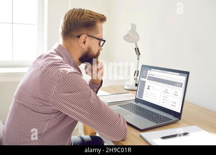 Der Geschäftsmann blickt beim Ausfüllen elektronischer Formulare oder Dokumente nachdenklich auf den Laptop-Bildschirm. Online-Banking. Stockfoto
