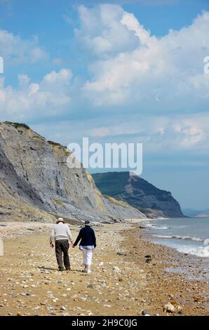 Ältere Männer und Frauen gehen Hand in Hand am strand von monmouth entlang bis zum Golden Cap charmouth dorset england Stockfoto