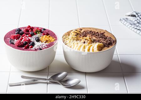 Smoothie-Schalen mit Schokolade und Beeren auf weißem Fliesengrund. Rohkost vegan Food-Konzept. Stockfoto