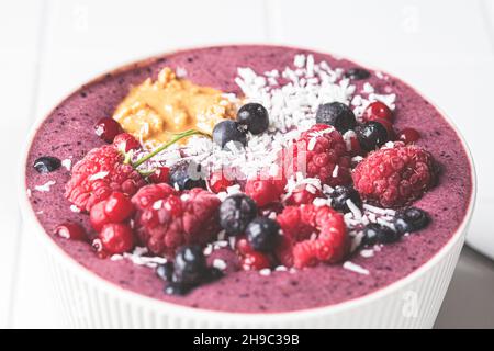 Berry Smoothie Schüssel mit Himbeeren, Erdnussbutter und Kokosnuss auf weißem Fliesenhintergrund, Nahaufnahme. Rohkost vegan Food-Konzept. Stockfoto