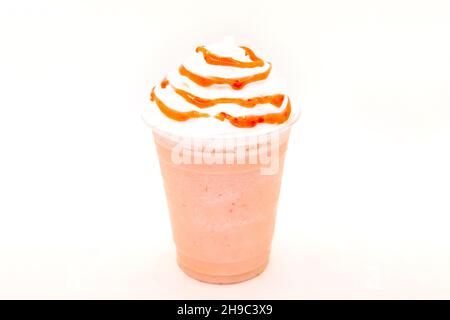 Erdbeermilch-Shake mit Sirup beträufelt auf Schlagsahne in einem Einweg-Plastikbecher. Stockfoto