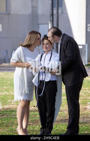 Jüdische Eltern gedenken der Bar Mitzvah ihres Sohnes mit einer Fotosession im Freien, bei der er einen tallis und Teffilin trägt. In einem Park in Queens NYC
