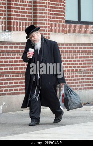 MULTITASKING. Ein orthodoxjüdischer Mann geht, telefoniert, trägt eine Tasche und trinkt Kaffee. In Williamsburg, Brooklyn, New York City. Stockfoto