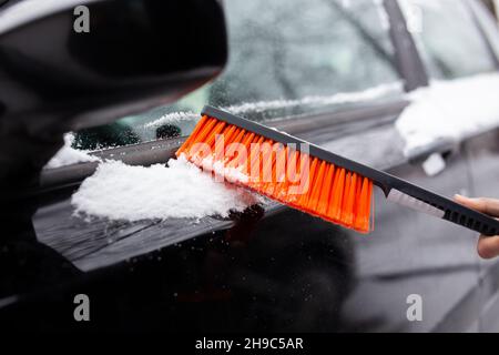 Winterprobleme mit dem Auto. Ein Mann reinigt das Auto mit einer Bürste vom Schnee Stockfoto