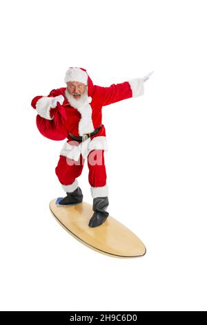 Porträt des emotionalen Weihnachtsmanns in rot-weißem Kostüm stehendes Surfbrett isoliert auf weißem Hintergrund. Konzept „Frohe Weihnachten“ Stockfoto