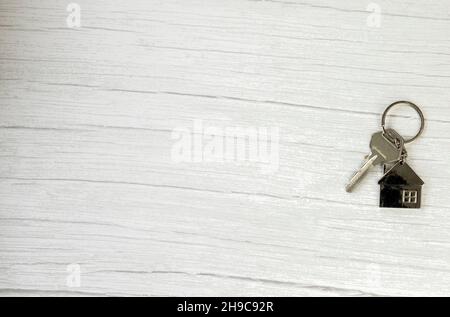 Silberner Schlüssel mit silberner Hausfigur auf weißem Holzhintergrund, Kauf neuer Haus Immobilien Konzept Kopie Raum Stockfoto