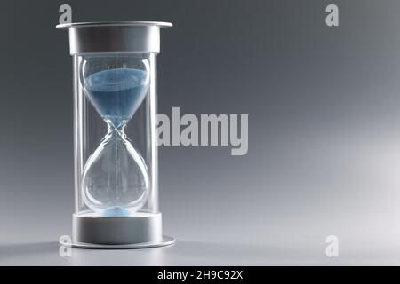 Nahaufnahme der Sanduhr mit blauem Sand auf grauem Hintergrund Stockfoto