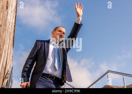 Selbstbewusster Geschäftsmann mittleren Alters mit Aktentasche, der die Treppe hoch läuft. Nahaufnahme eines Geschäftsmannes in einem blauen Anzug mit Tasche, der die Treppe hinunter ging Stockfoto