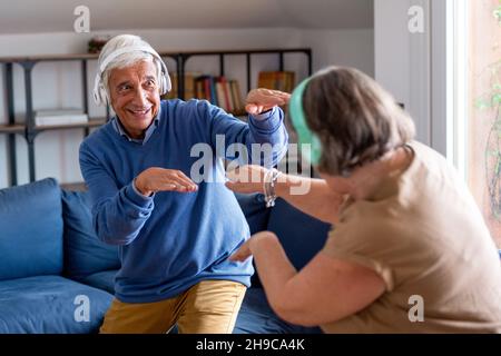 Seniorenpaar zu Hause. Schöner alter Mann und attraktive alte Frau verbringen gerne Zeit zusammen. Spaß haben und tanzen mit kabellosen Kopfhörern Stockfoto