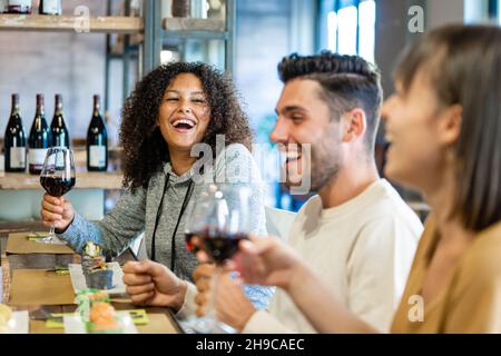 Eine Gruppe junger Leute, die im Restaurant zu Mittag essen, Millennials, die an einem Festtag gemeinsam Spaß haben und mit einem Glas Rotwein toasten Stockfoto