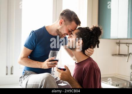 Zärtlichkeit Moment des lächelnden schwulen Paares, junger Mann toasten mit Rotwein in der Küche, männliche Paar Spaß und trinken Rotwein zum Feiern Stockfoto