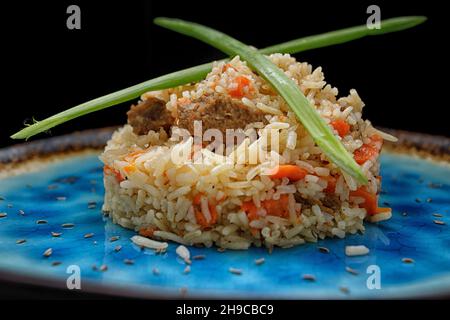 Usbekischer Pilaf auf blauem Teller, auf dunklem Hintergrund Stockfoto