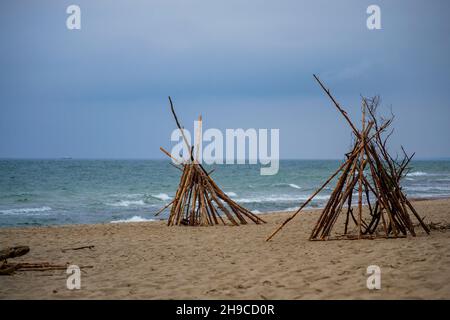 Der sandige Strand des Meeres und die Tipies, die aus dem Holz gesammelt wurden, das auf die Küste im Nationalpark Kurische Nehrung geworfen wurde Stockfoto