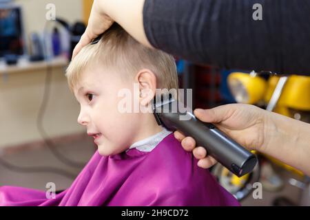 Ein kleiner Junge sitzt in einem Kinderfriseur, um sich die Haare zu schneiden. Stockfoto