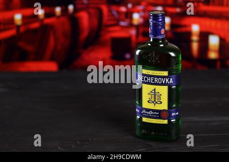 CHARKOW, UKRAINE - 14. FEBRUAR 2021: Kräuterlikör-Flasche Becherovka auf Holztisch mit roter Bar im Hintergrund. Elite-Alkoholproduktion Stockfoto