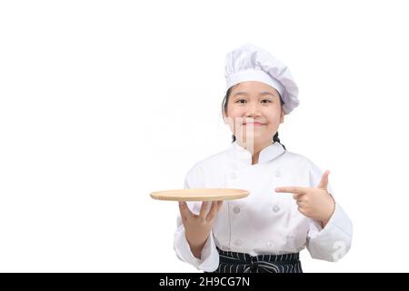 Nettes Mädchen Koch hält Holzplatte und zeigt ihren Finger auf Platte isoliert auf weißem Hintergrund. Food-Menü Präsentation Konzept Stockfoto