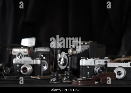 CHARKOV, UKRAINE - 27. APRIL 2021: Filmkameras und eine andere alte Retro-Fotoausrüstung auf schwarzem Holztisch in der Dunkelkammer des Fotografen. Foto Stockfoto