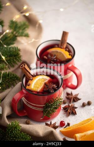 Zwei Tassen Glühwein mit orangefarbenen Keilen und Gewürzen, umgeben von weihnachtlicher Dekoration Stockfoto