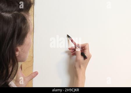 Der Künstler zeichnet mit Bleistift auf eine weiße Leinwand. Blick hinter die Schulter. Zeichnen mit Aquarellen in einem Home Art Studio. Stockfoto