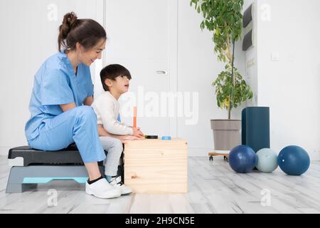 Therapeut tun Entwicklungsaktivitäten mit einem kleinen Jungen mit zerebraler Lähmung, mit Rehabilitation, Lernen . Ausbildung im medizinischen Versorgungszentrum. Hochwertige Fotos. Stockfoto