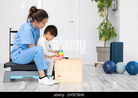 Therapeut tun Entwicklungsaktivitäten mit einem kleinen Jungen mit zerebraler Lähmung, mit Rehabilitation, Lernen . Ausbildung im medizinischen Versorgungszentrum. Hochwertige Fotos. Stockfoto